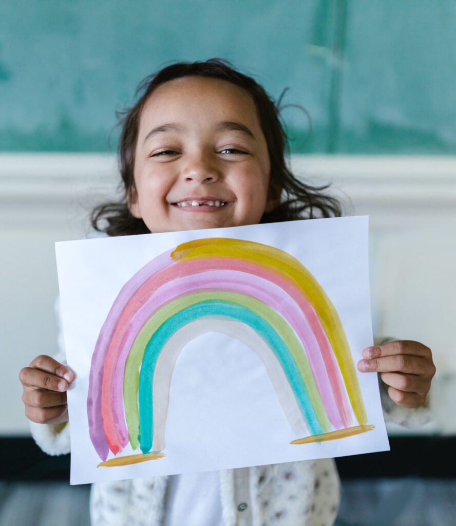 young girl holding watercolor painting of a rainbow